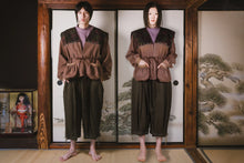 Person wearing a brown outfit standing in front of a traditional Japanese sliding door with a painting.