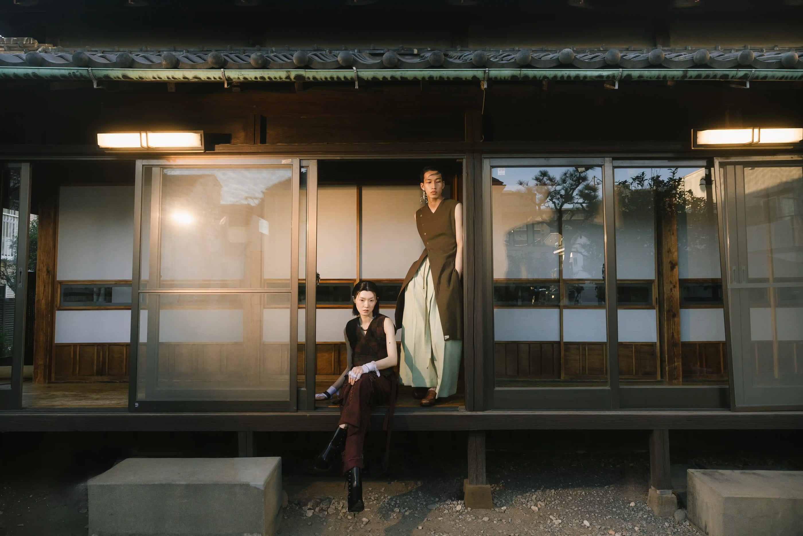 Two women standing on a traditional Japanese veranda with a modern house in the background.