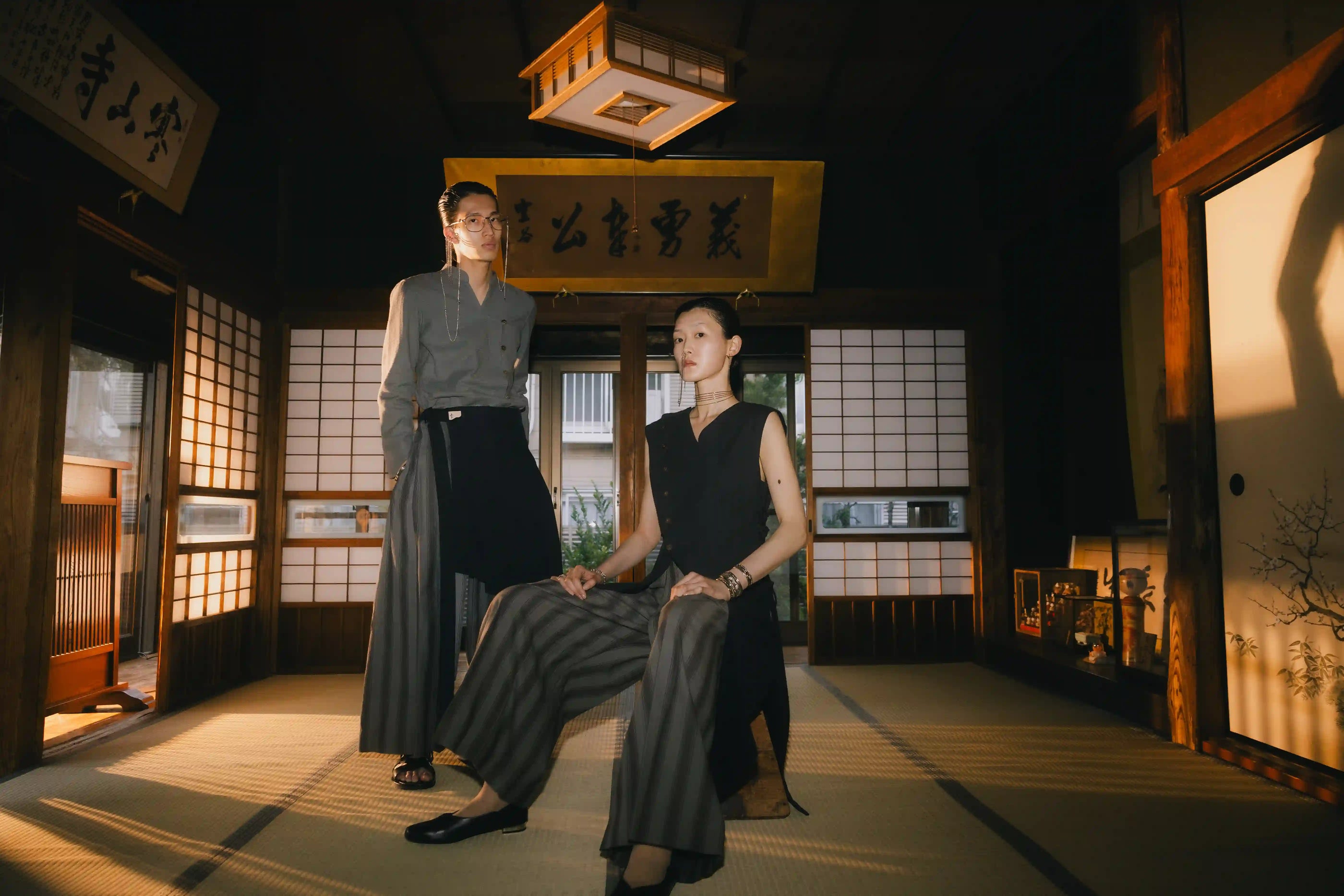 Two individuals in traditional attire in a Japanese-style room with wooden floors and sliding doors.