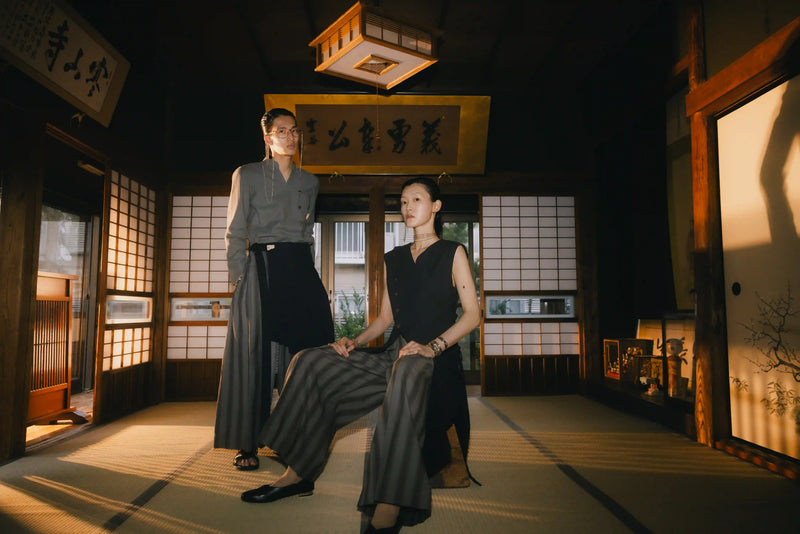 Two individuals in traditional attire in a Japanese-style room with wooden floors and sliding doors.